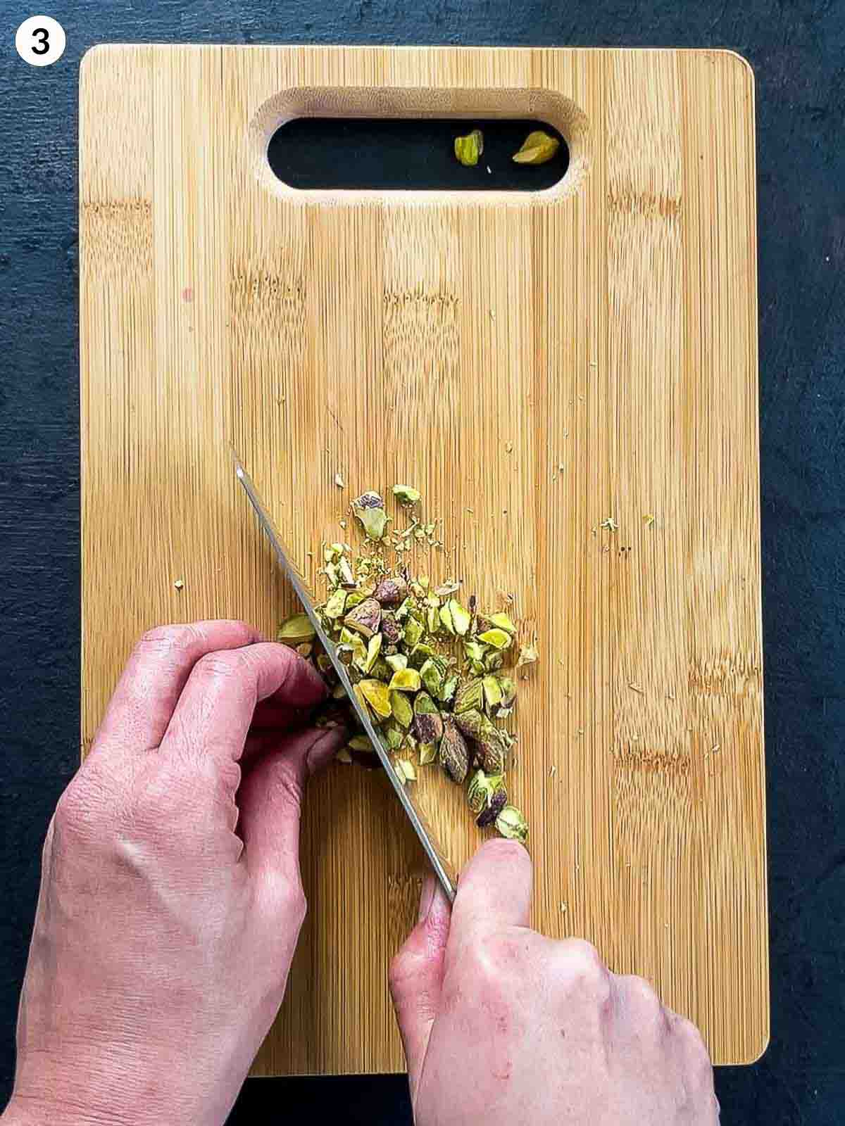 Chopping pistachio nuts with a knife on a wooden board
