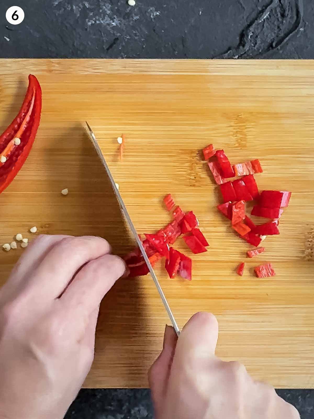 cutting chilli with a knife on a wooden chopping board