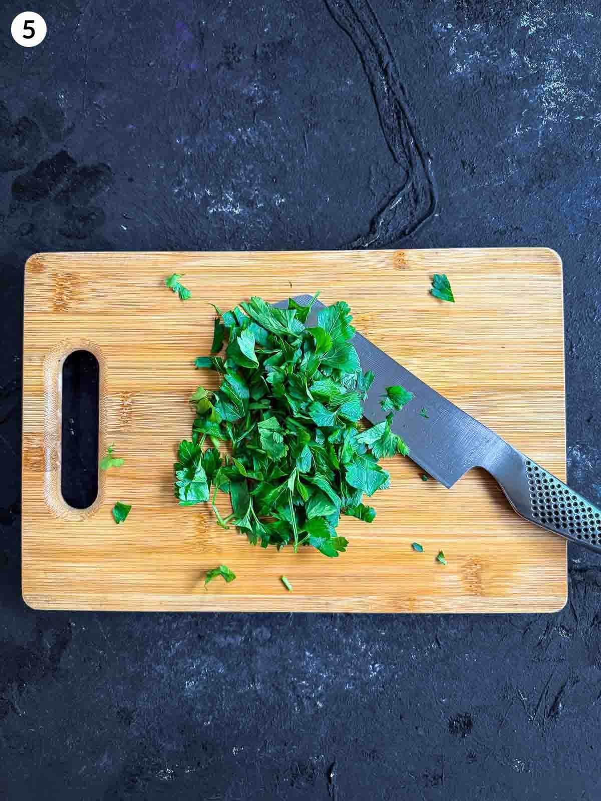 cutting parsley with a knife on a wooden chopping board