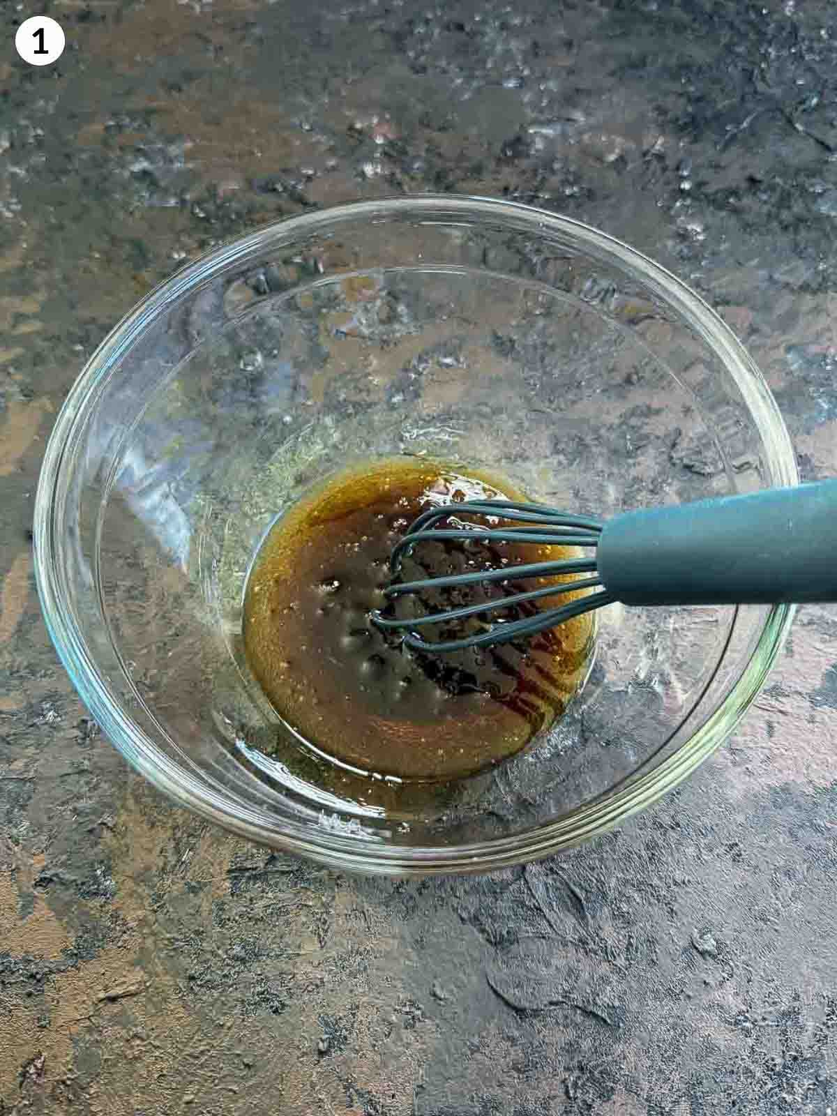 mixing salad dressing in a clear bowl with a whisk