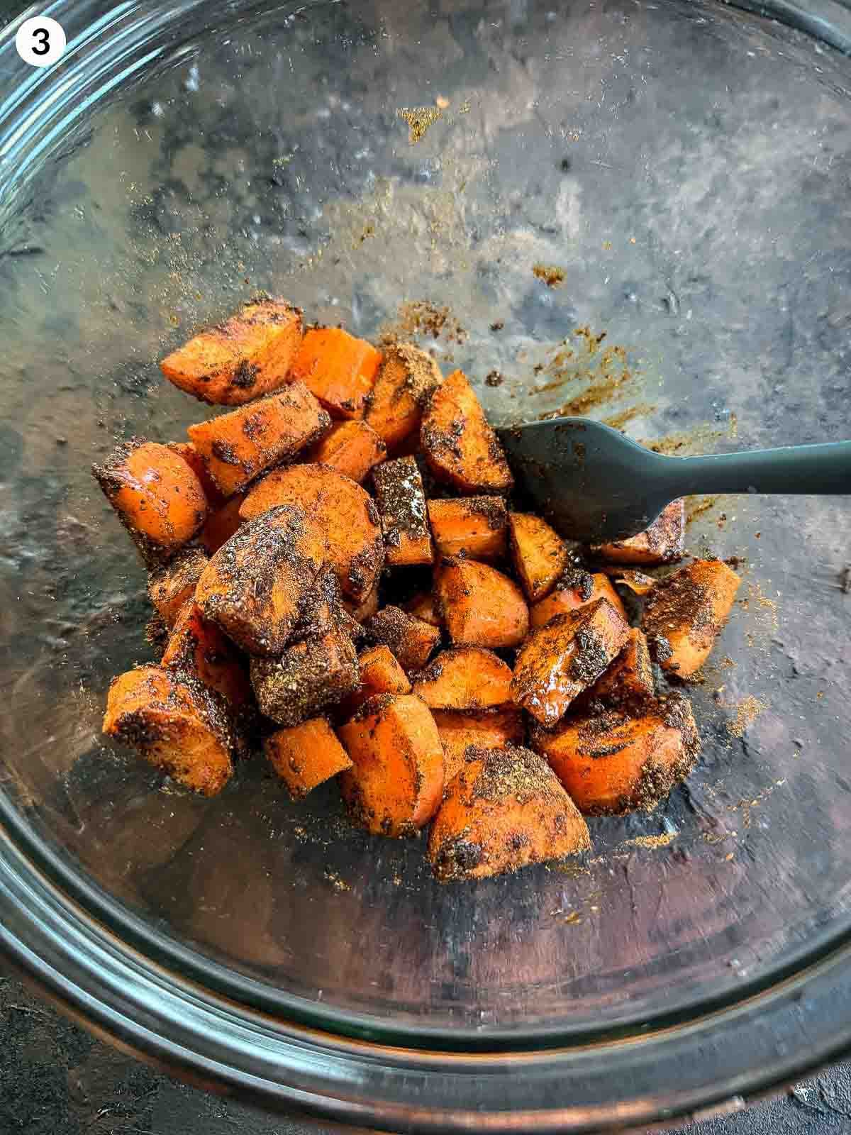 mixing baharat spice with carrots in a clear bowl with a spatula