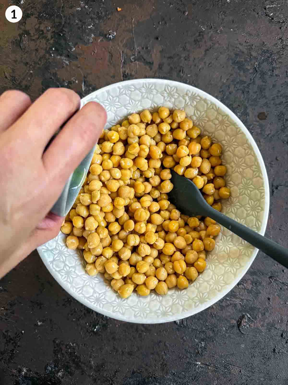 adding olive oil into a bowl of chickpeas and mixing with a spatula