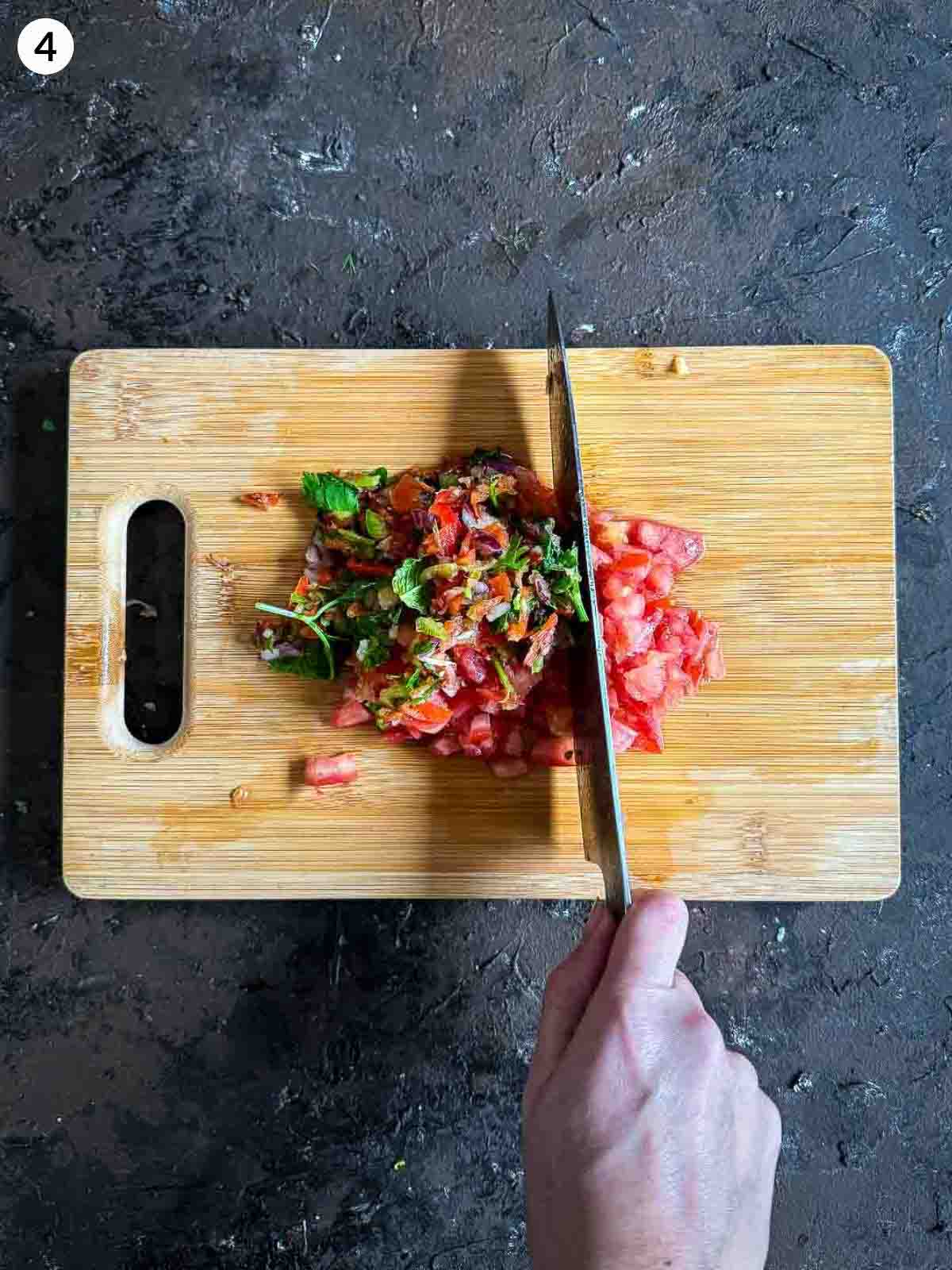 chopping ingredients for ezme salad with a knife on a wooden board