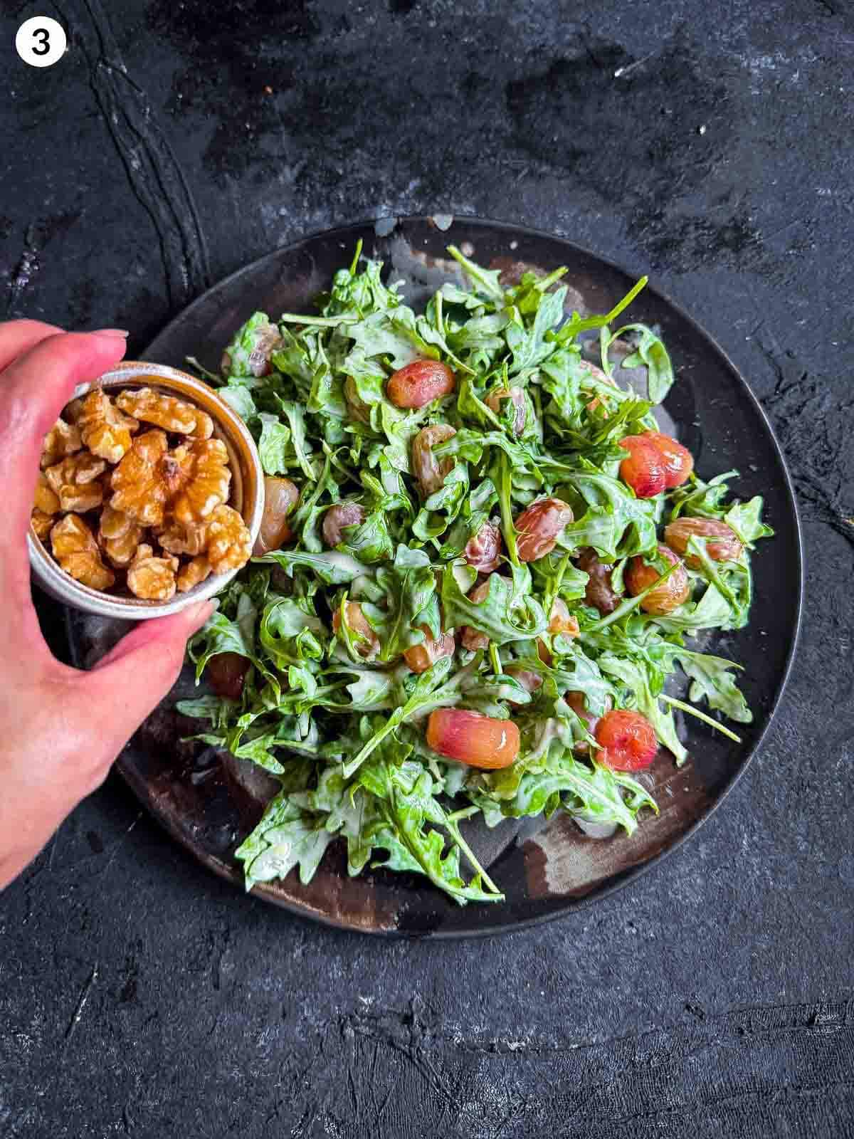 adding walnuts to a plate of Warm Arugula and Roasted Grape Salad with Blue Cheese