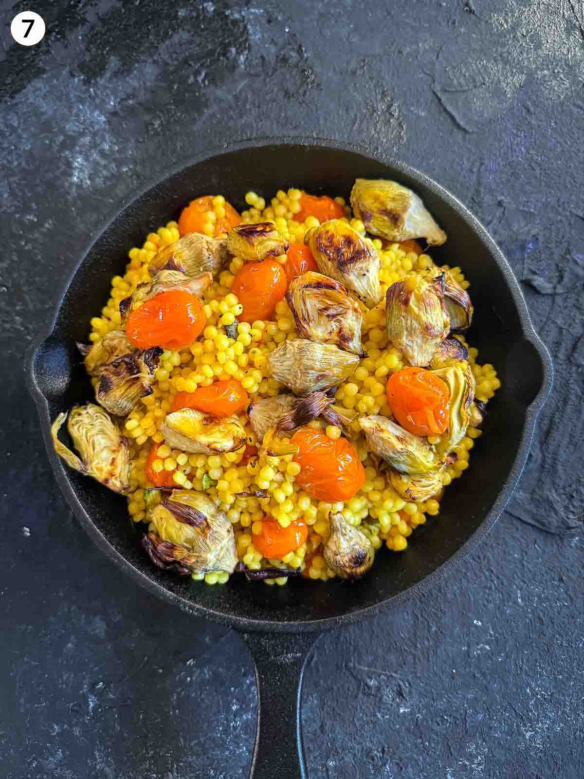 assembling Saffron Israeli Couscous with Roasted Artichoke Hearts in a cast iron pan