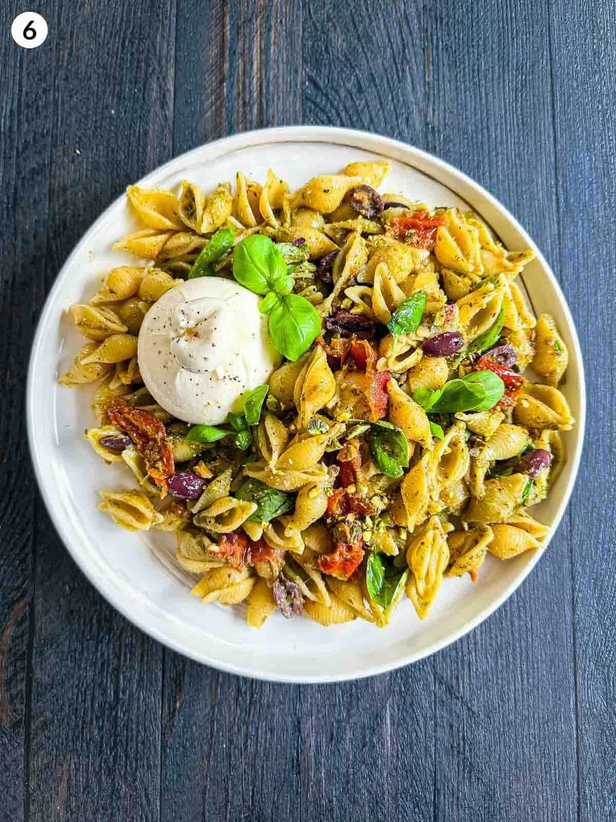 Semi-dried Tomato Pesto Pasta Salad with Burrata on a white plate against a dark background