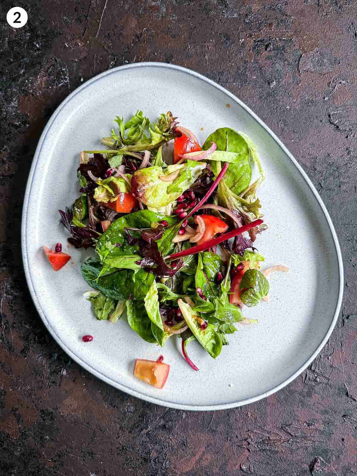 salad leaves and tomatoes on a grey platter against a dark background