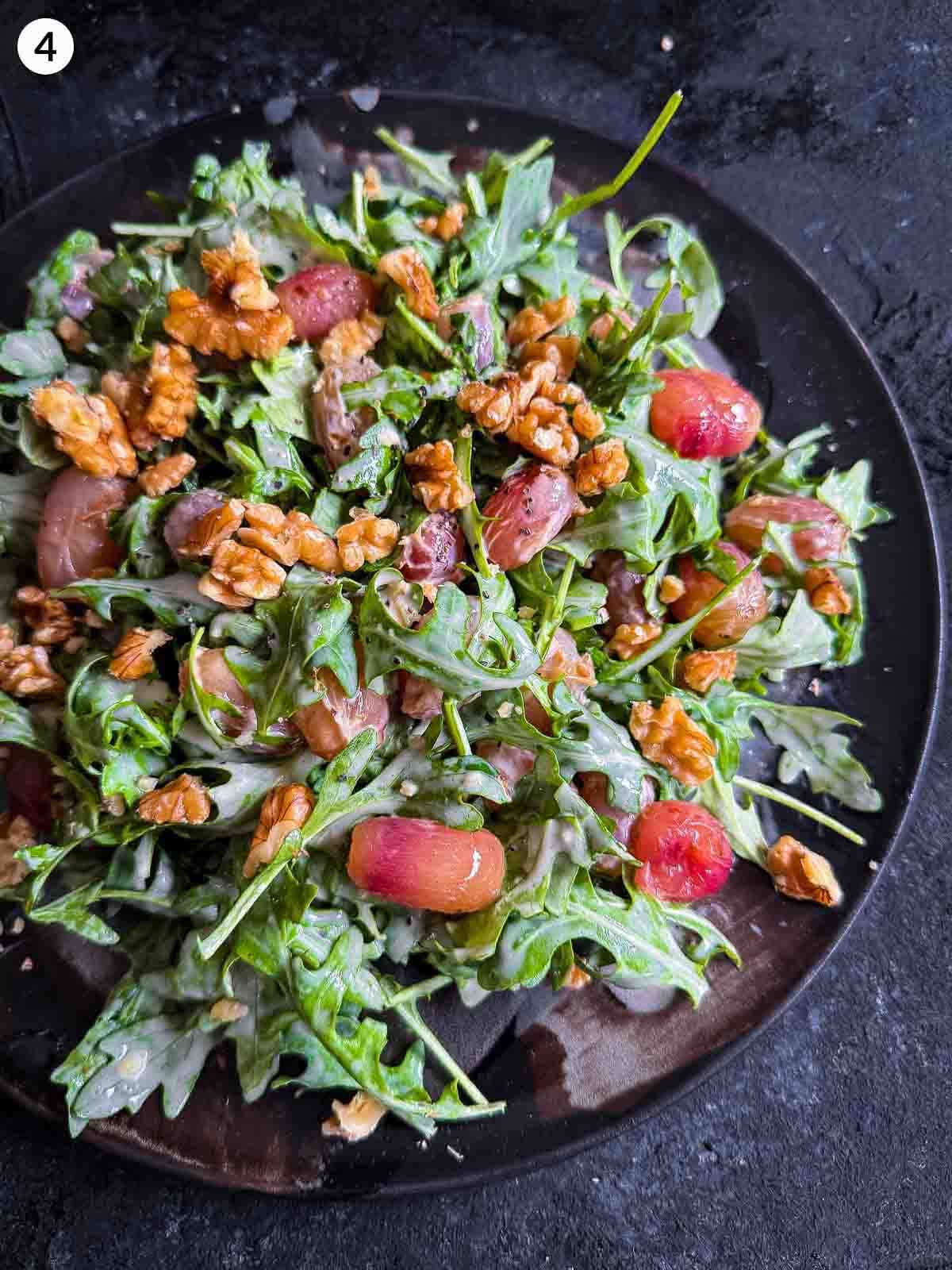 Warm Arugula and Roasted Grape Salad with Blue Cheese on a dark plate against a dark background