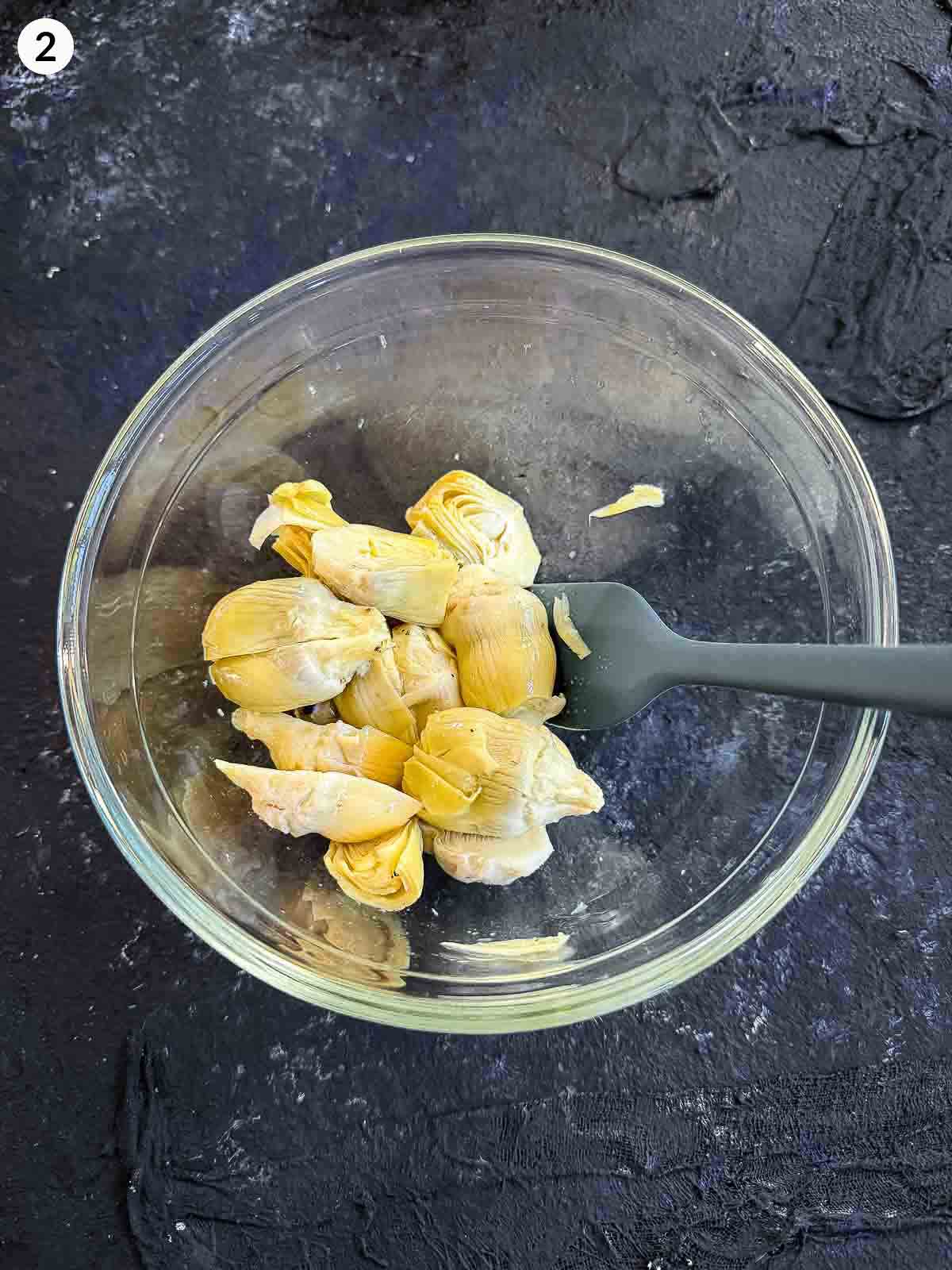 artichoke hearts in a clear bowl with a grey spatula