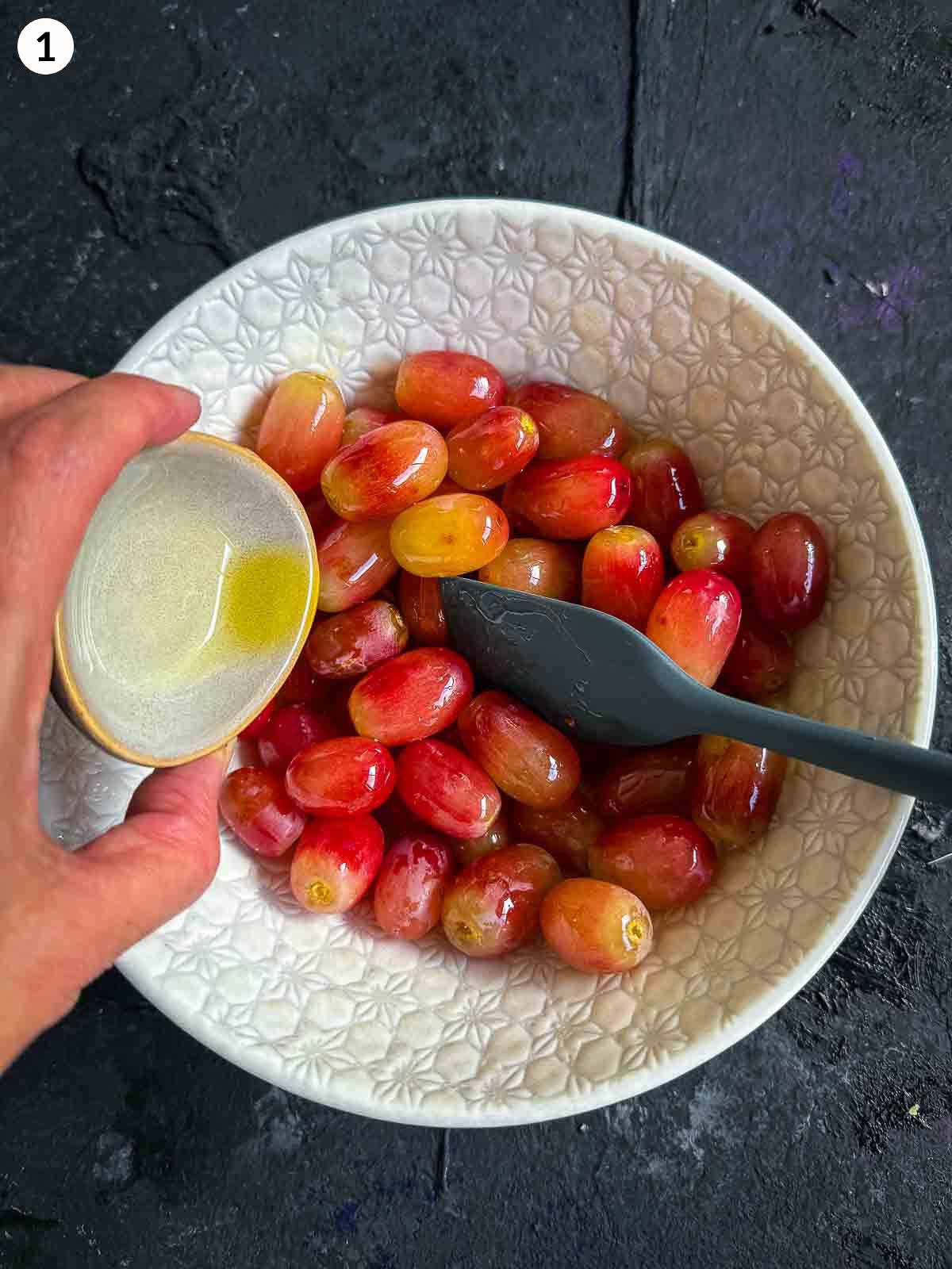 adding olive oil to a bowl of red grapes with a spatula