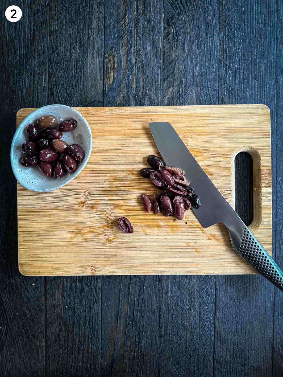 Chopping black olives with a knife on a wooden board