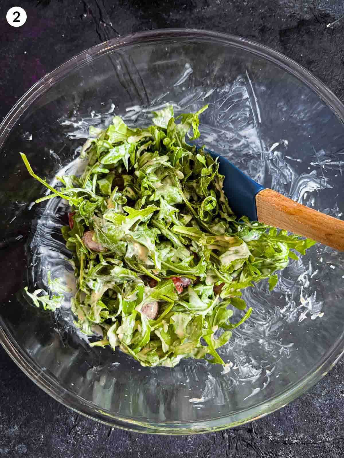 tossing ingredients for Warm Arugula and Roasted Grape Salad with Blue Cheese in a bowl with a spatula